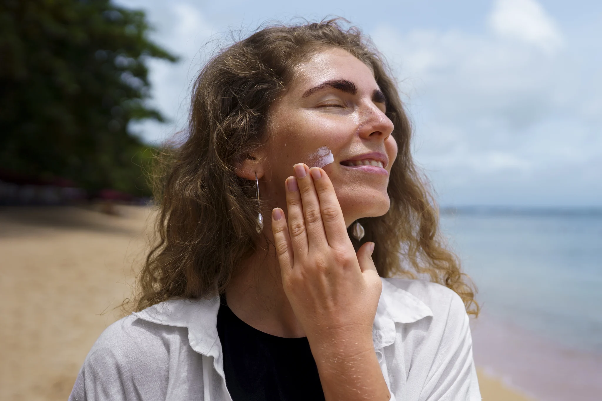 Imagem de uma mulher passando protetor solar na praia para cuidar da pele no verão